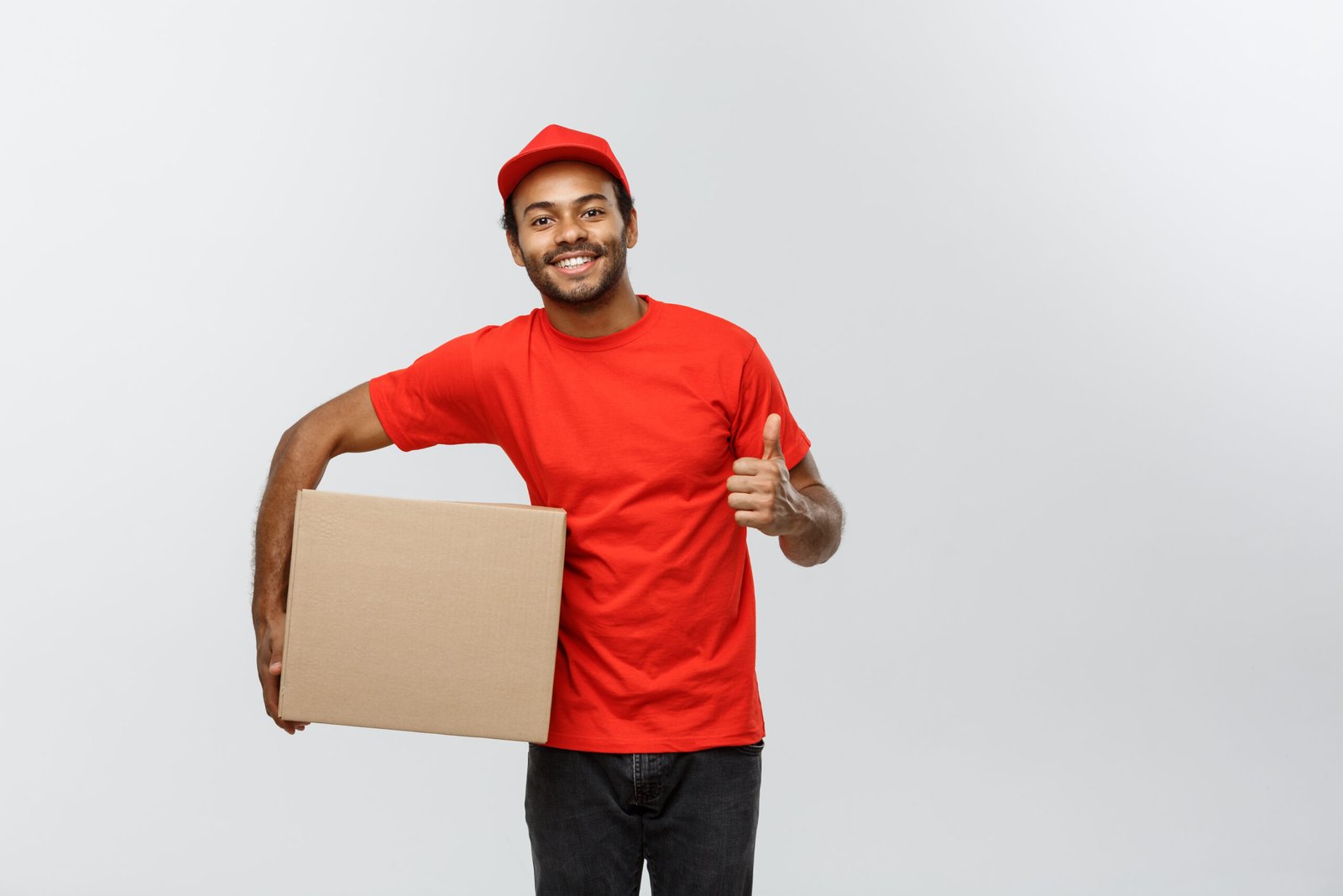 delivery concept portrait of happy african american delivery man holding a box package and showing thumps up. isolated on grey studio background. copy space.